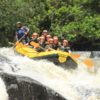 Bote da Brotas rafting com sete pessoas sentadas no piso do bote descendo uma queda