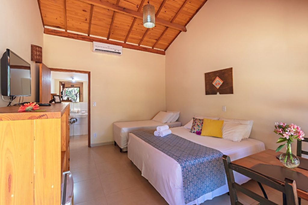 interno-do-quarto-com-camas-de-casal-e-solteiro,-mesa-com-duas-cadeiras-e-tv-naparede-oposta-as-camas