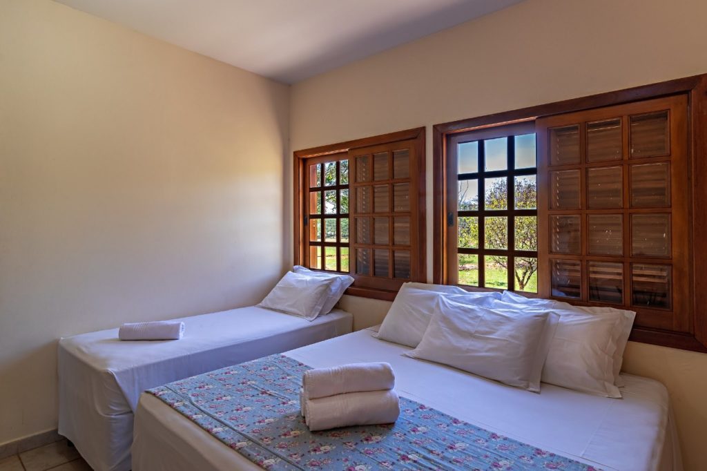 quarto-com-camas-de-casal-e-solteiro-abaixo-das-janelas-com-vista-para-área-verde